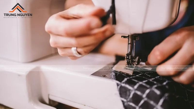 Một người đang tập trung may vá bằng tay trong điều kiện ánh sáng yếu vào buổi tối.