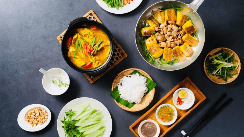 Món chả cá Lã Vọng đang được chiên trên chảo nóng với hành và thì là, ăn kèm bún, lạc rang và rau thơm
